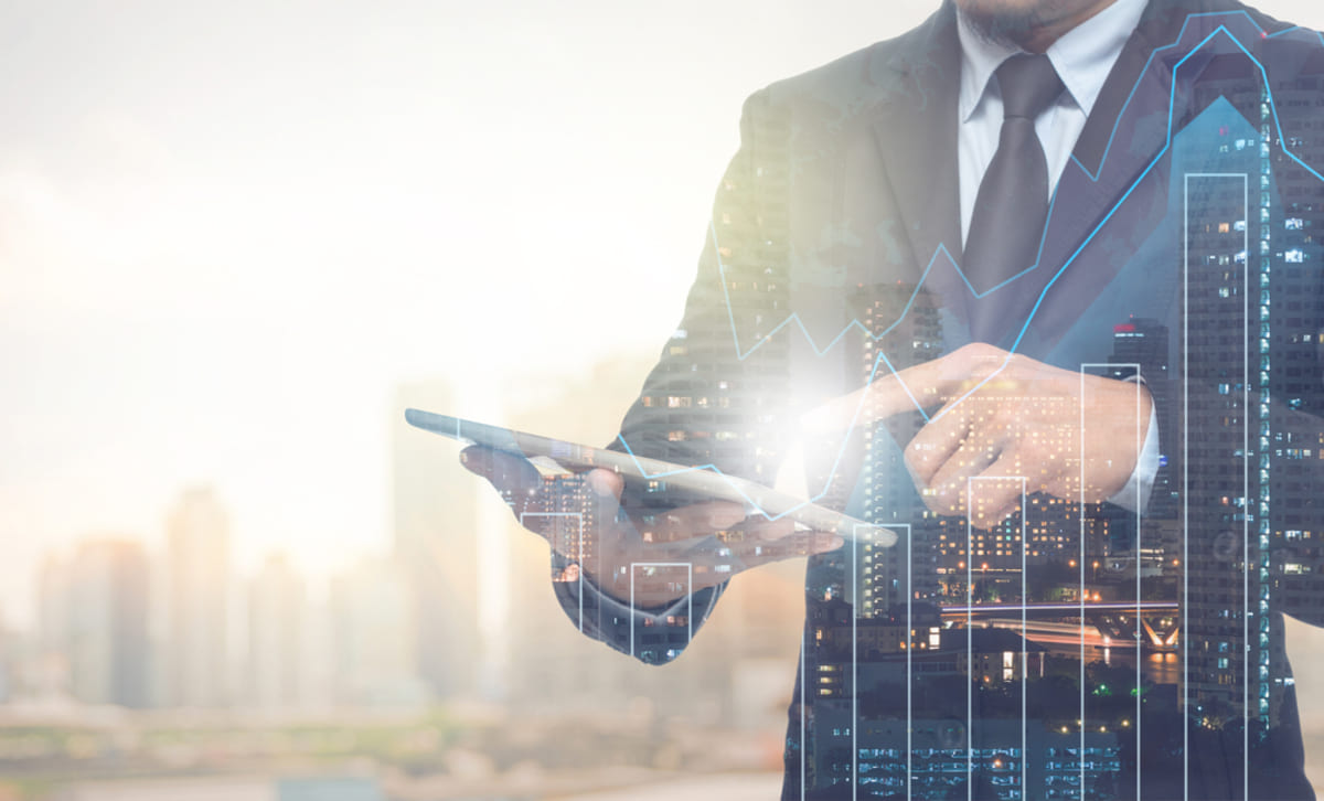 Double exposure of businessman using tablet with cityscape and financial graph on blurred building background