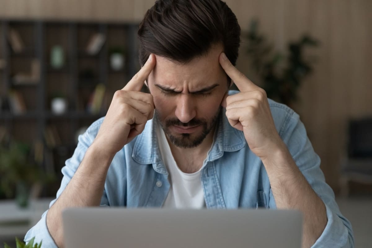 Stressed male sit by pc contemplate think hard with closed eyes touch forehead with fingers